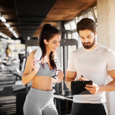 Frau trainiert mit Trainer im Fitnessstudio